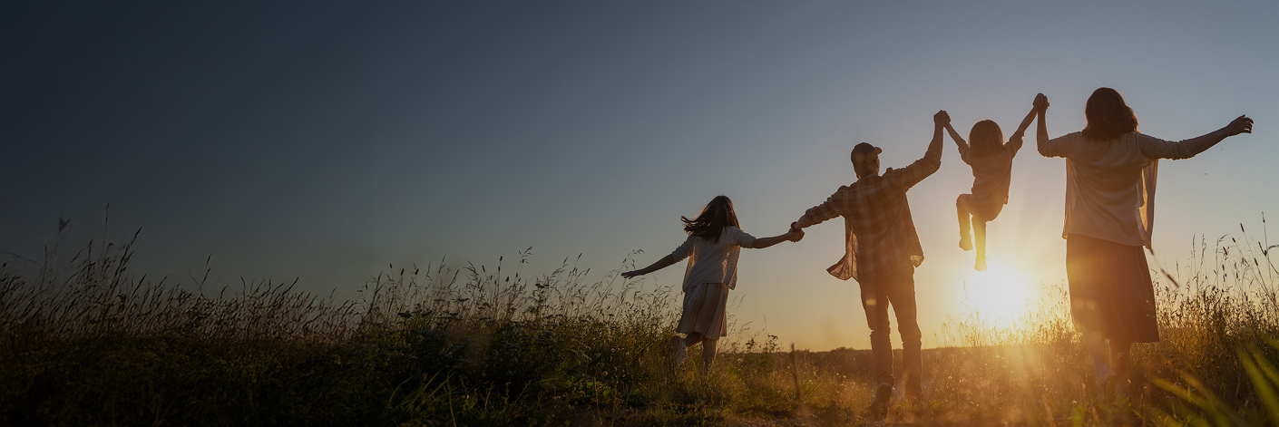 Silhouette of a family with two adults and two children with arms raised at sunset