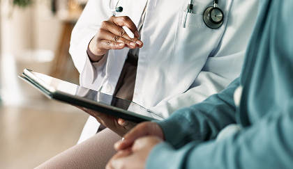 A doctor in a white coat shows a patient something on an iPad
